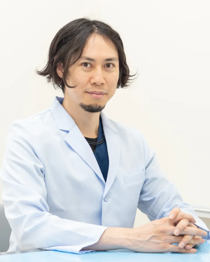白衣を着て診察机に着く院長 丹羽昭博